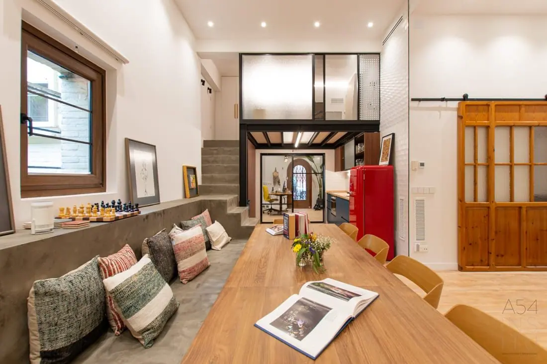 Sala con mesa larga de madera, banco con cojines y la escalera al fondo