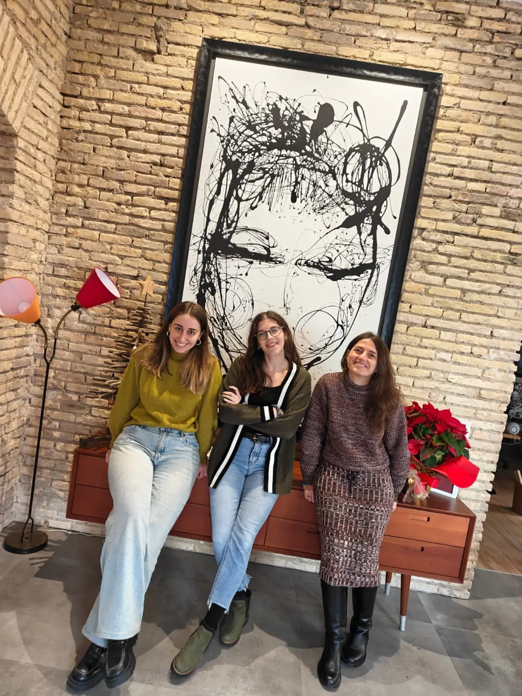 Tres trobadoras sentadas en un banco bajo un gran cuadro